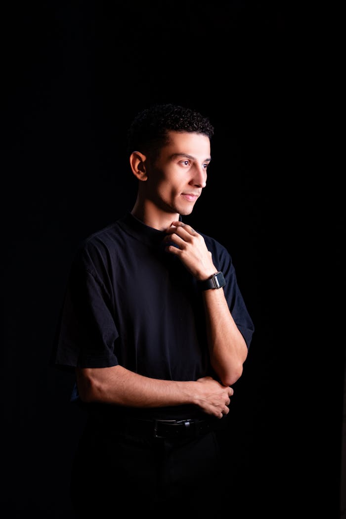 Studio portrait of a thoughtful man in black attire, showcasing modern fashion and accessories.