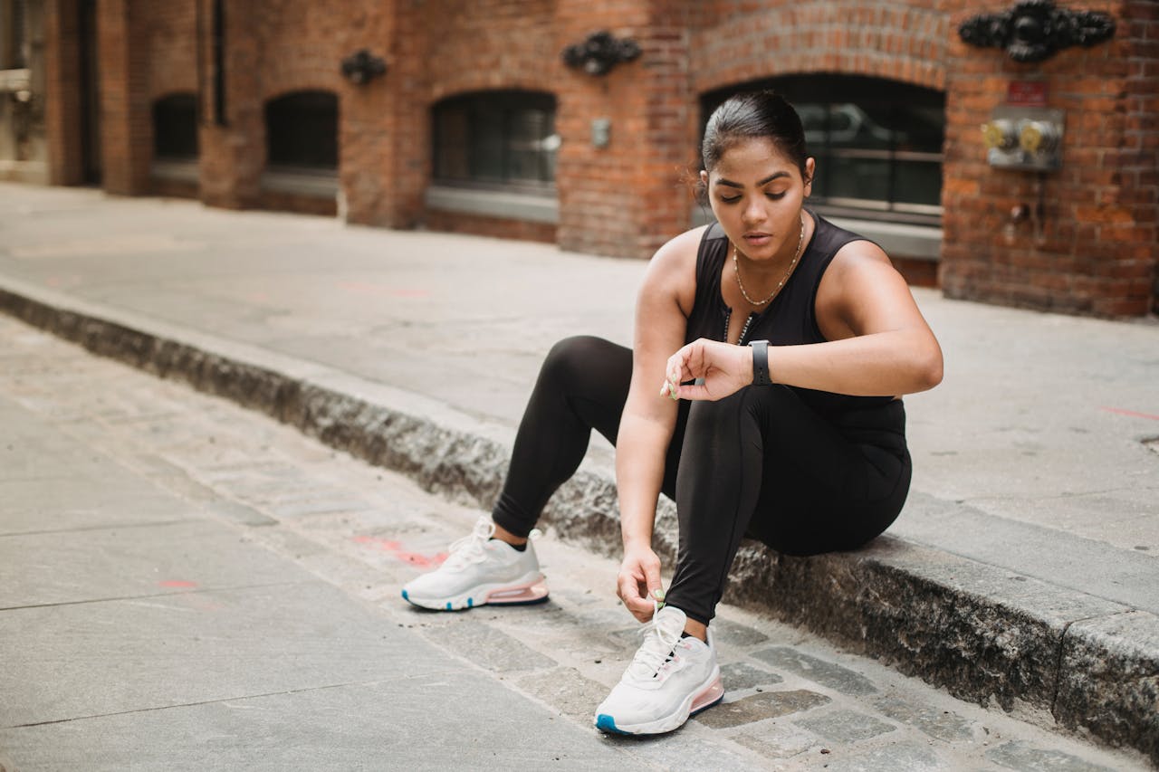 about-us Woman in activewear checking smartwatch while sitting on urban sidewalk.